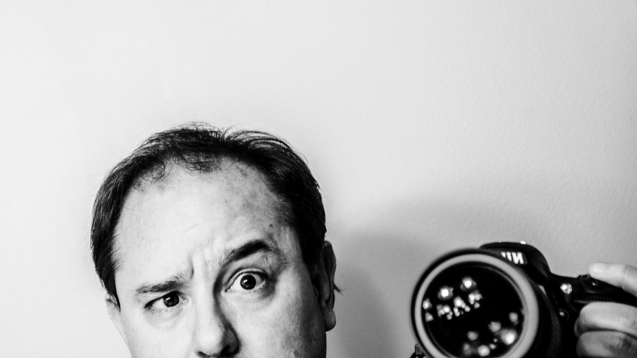 A black and white photograph of John Scalzi taking a photograph of himself, pulling a funny face