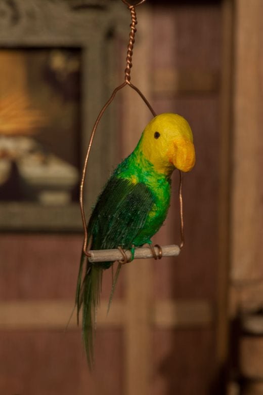 tiny version of a green and yellow parrot, complete with feathers, sitting on a perch
