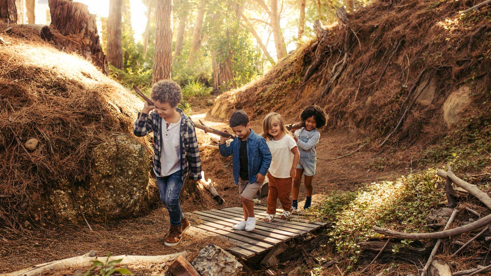 Four children in a forest working together to carry a large log up a path