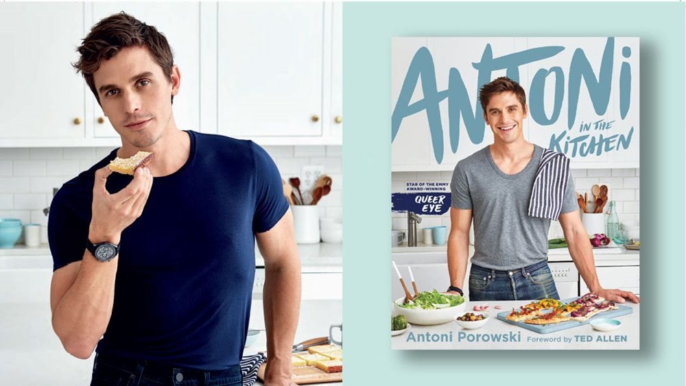 Antoni in a kitchen eating some bread alongside a copy of his book, Antoni in the Kitchen