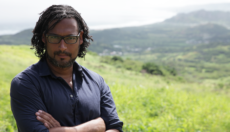 David Olusoga standing with arms folded in a field. 