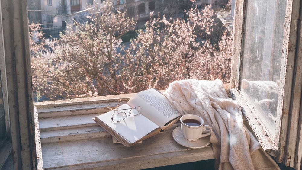 Book and coffee on windowsill with blossoms outside