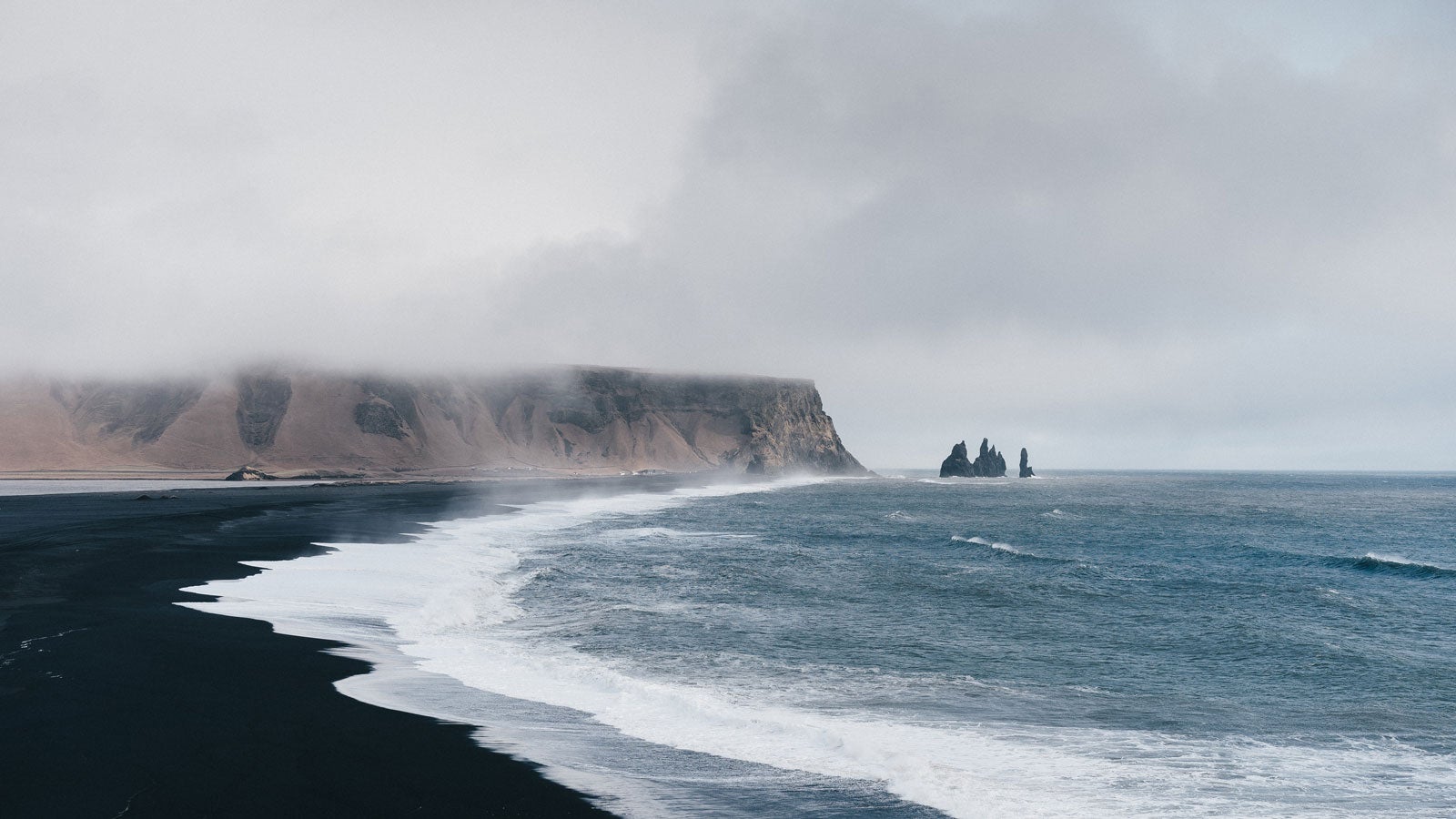 Icelandic beach with black sand and mist hanging over mountains in the far distance