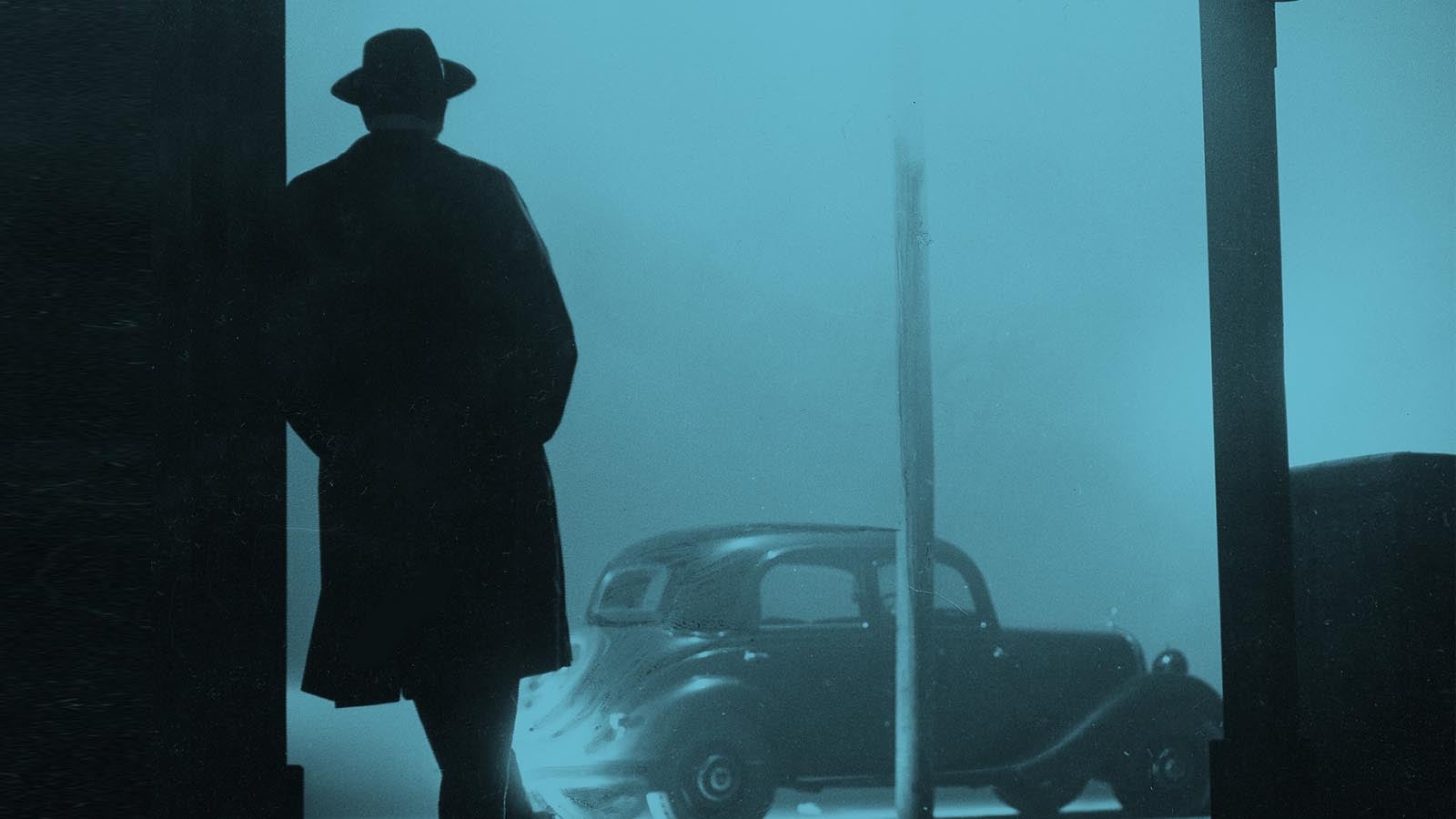 Silhouette of a man in the 1950s , wearing a wide-brimmed hat and looking out toward an old car on a misty evening