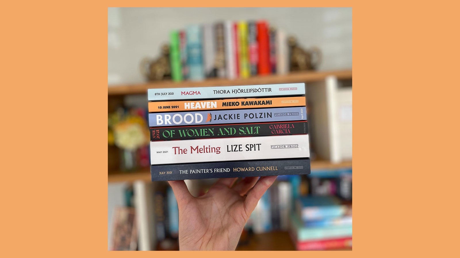 A photograph of a hand wielding a stack of books in front of a blurred out bookcase, on an orange background. A photograph of a hand wielding a stack of books in front of a blurred out bookcase, on an orange background.