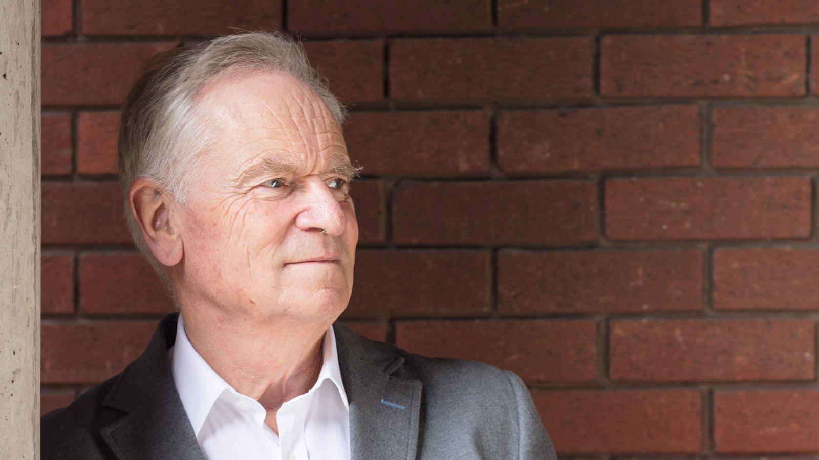 Jeffrey Archer looking away from the camera, standing in front of a brick wall