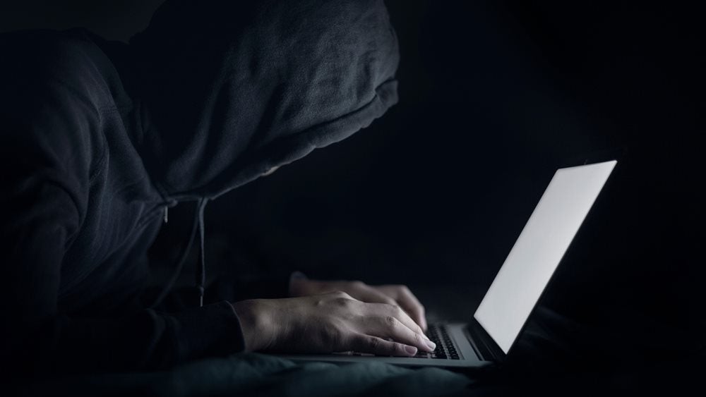 Man wearing a hoodie hunched over laptop in the dark