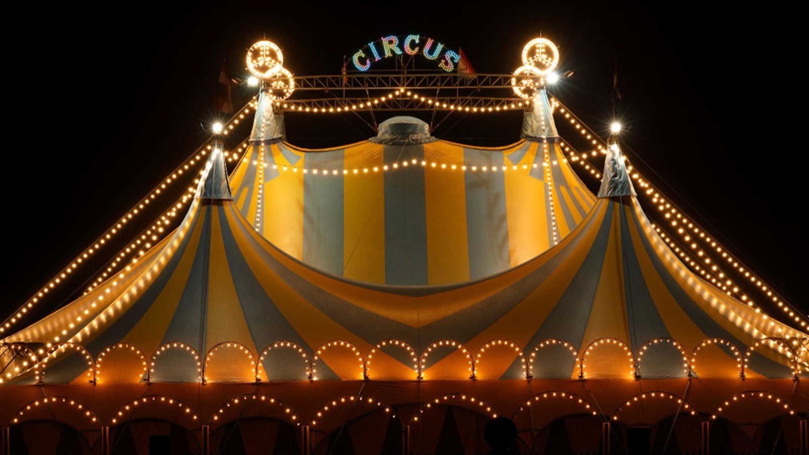 Blue and yellow circus tent with a light up circus sign on top at night