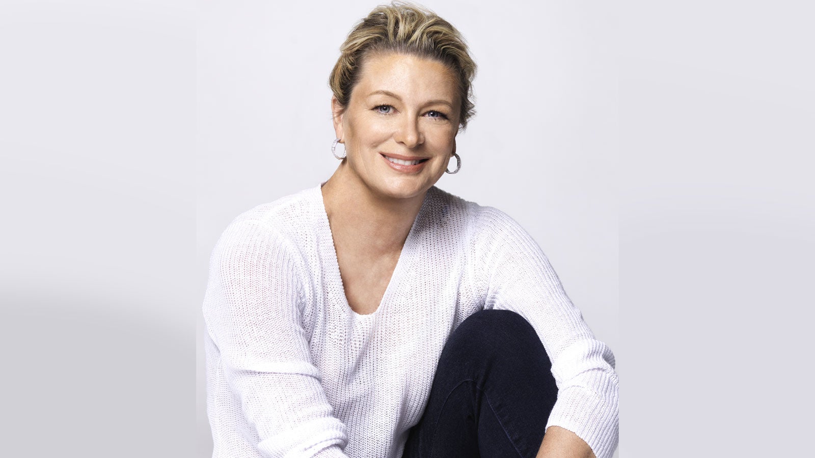 Kristin Hannah smiling wearing a white jumper in front of a white background