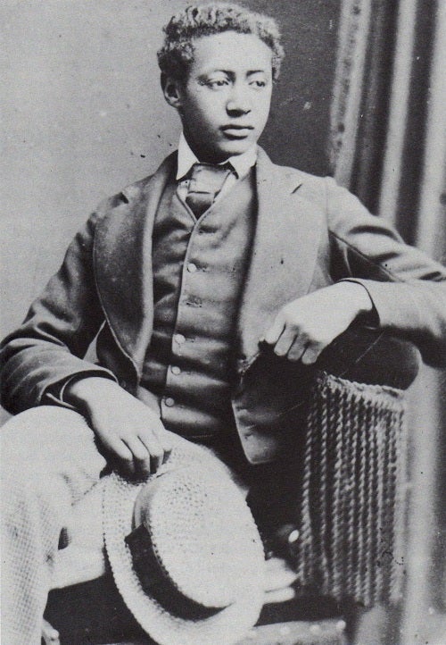 A black and white photograph of Dejazmatch Alemayehu Tewodros, seated, wearing a western suit, looking away from the camera and holding his hat