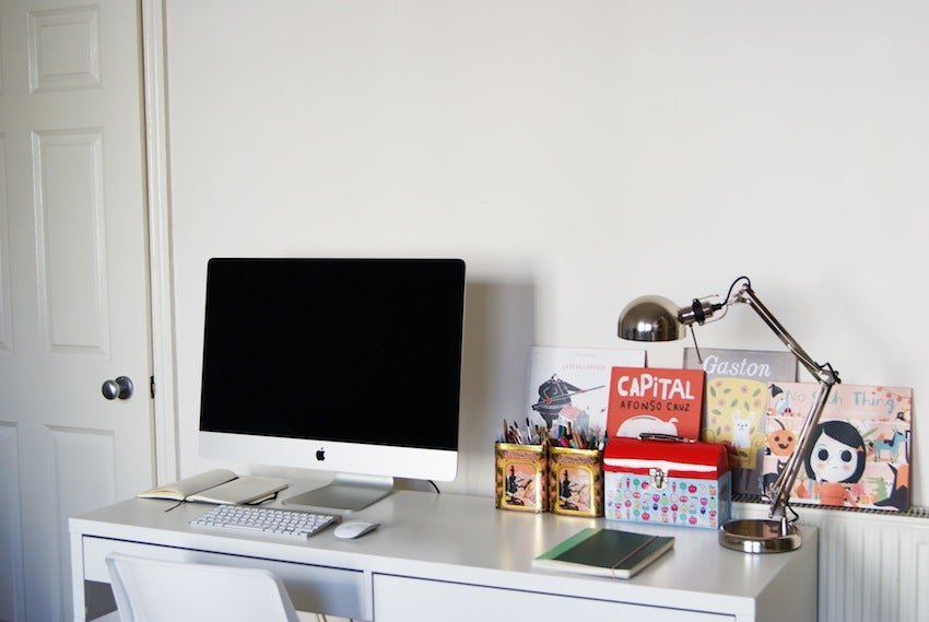 Clean white desk with and Apple computer and children's books stacked to the left