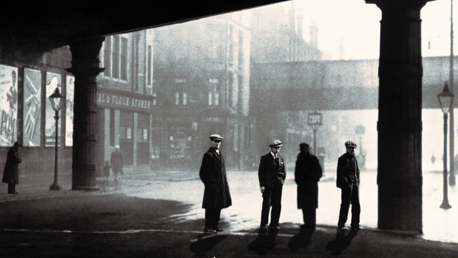 Black and white photograph of four men wearing wool coats and flat caps on the streets of 1930s Glasgow