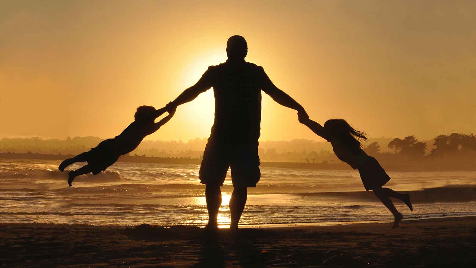 a man holding two children children by the hands and playing on the beach at sunset