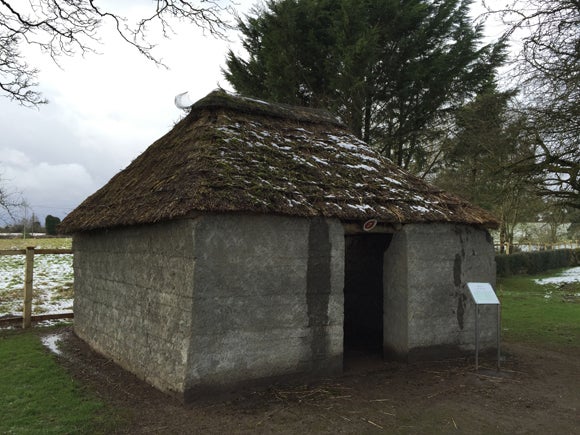 small home in a field, with a thatch roof, earthen walls, no windows and a simple opening for a door, in a small field with snow on the ground