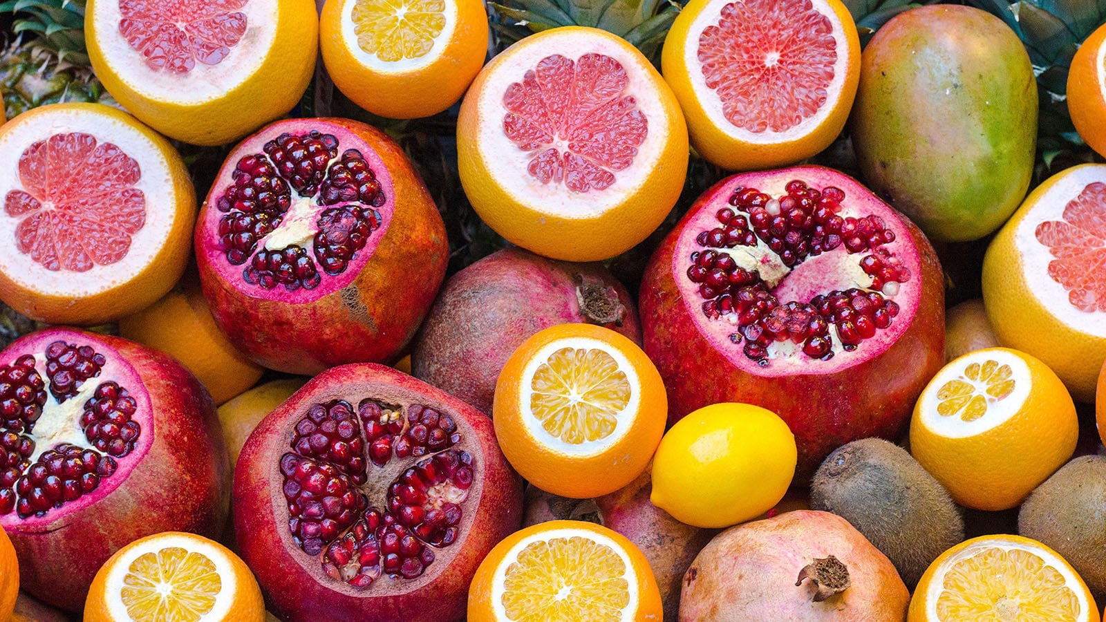pomegranates oranges and grapefruit fill the image - some fruit have top cut off to show colourful seeds
