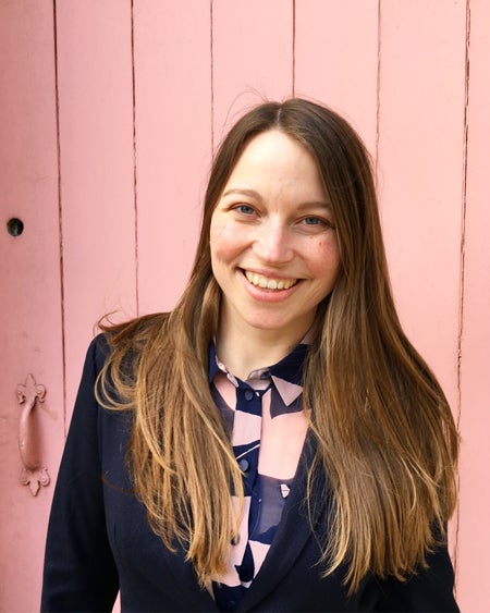 Photograph of Erica Gillingham smiling to camera wearing a navy jacket in front of a pink door