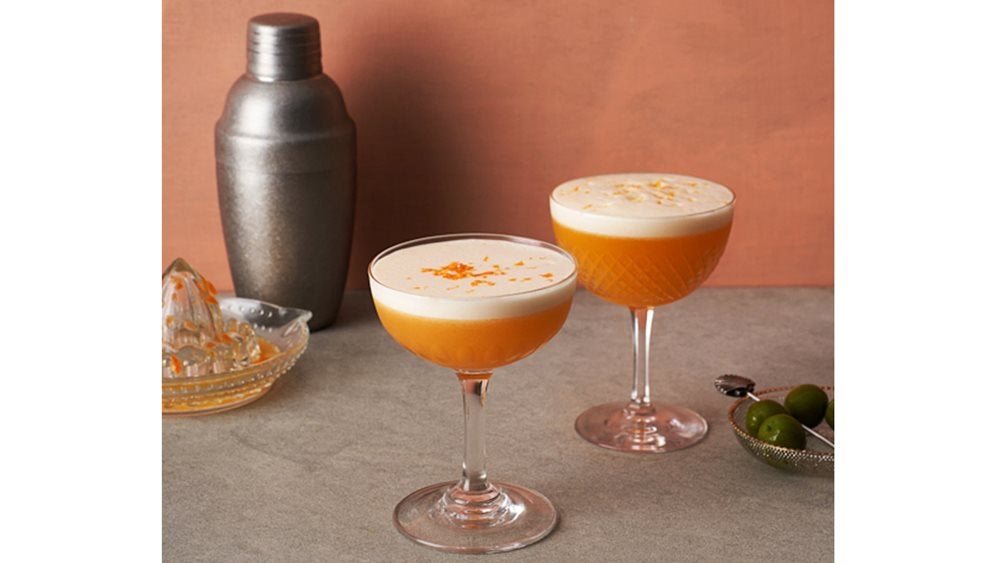 Two glasses of marmalade sour cocktail next to a cocktail shaker