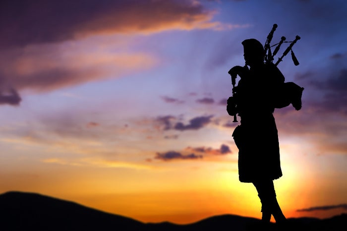 Silhouette of a man playing the bagpipes against the background of a sunset