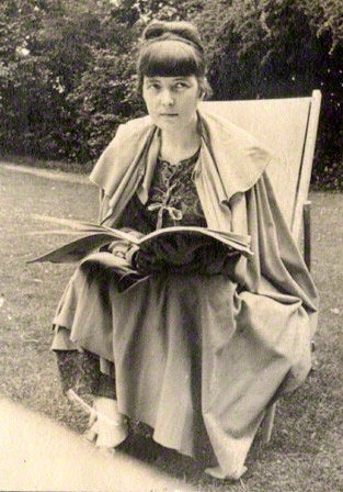 A black and whte photograph of Katherine Mansfield in 1917, sitting reading on a deck chair in a garden