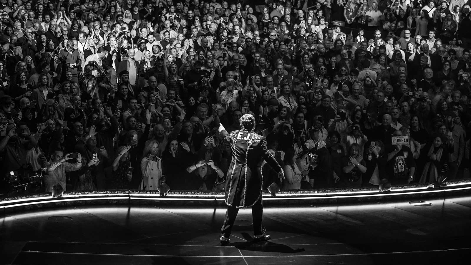 Black and white photograph of Elton John in front of a large crowd