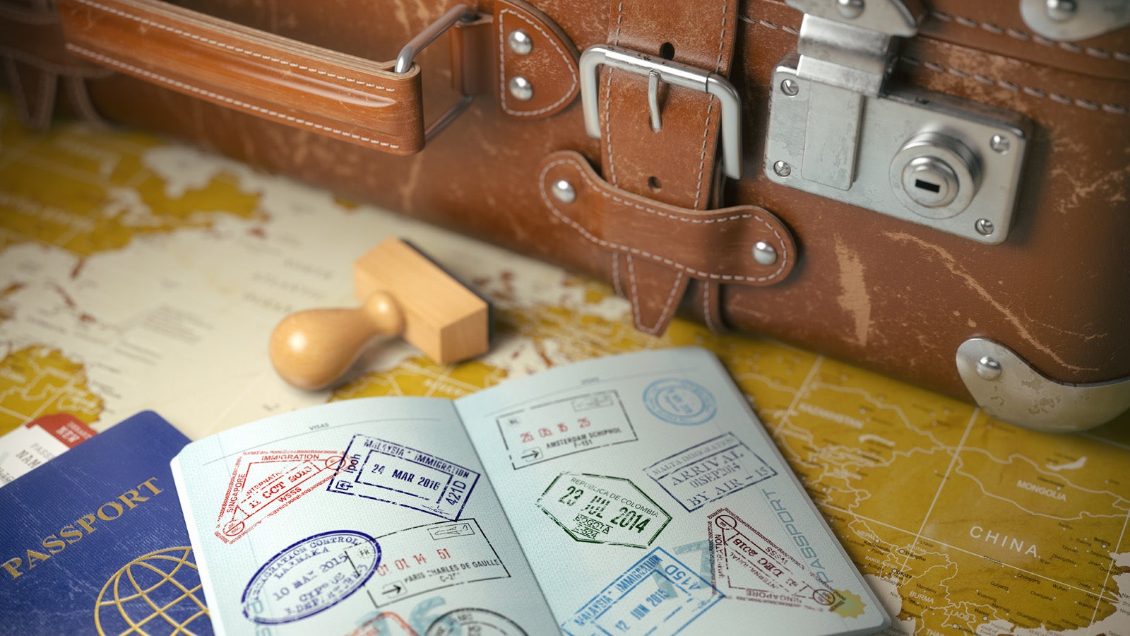 A suitcase next to an open passport showing lots of stamps