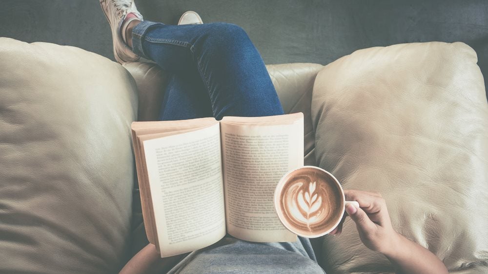 Person reading a book with coffee on sofa
