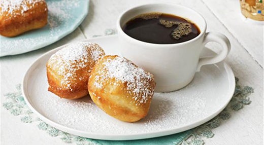 two beignets with cup of black coffee on plate