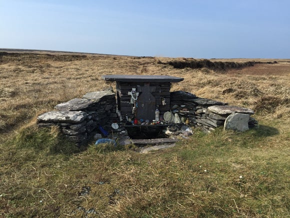 A small structure with a well at its centre and stones piled either side. Above it, people have placed many crosses and figures of The Virgin Mary