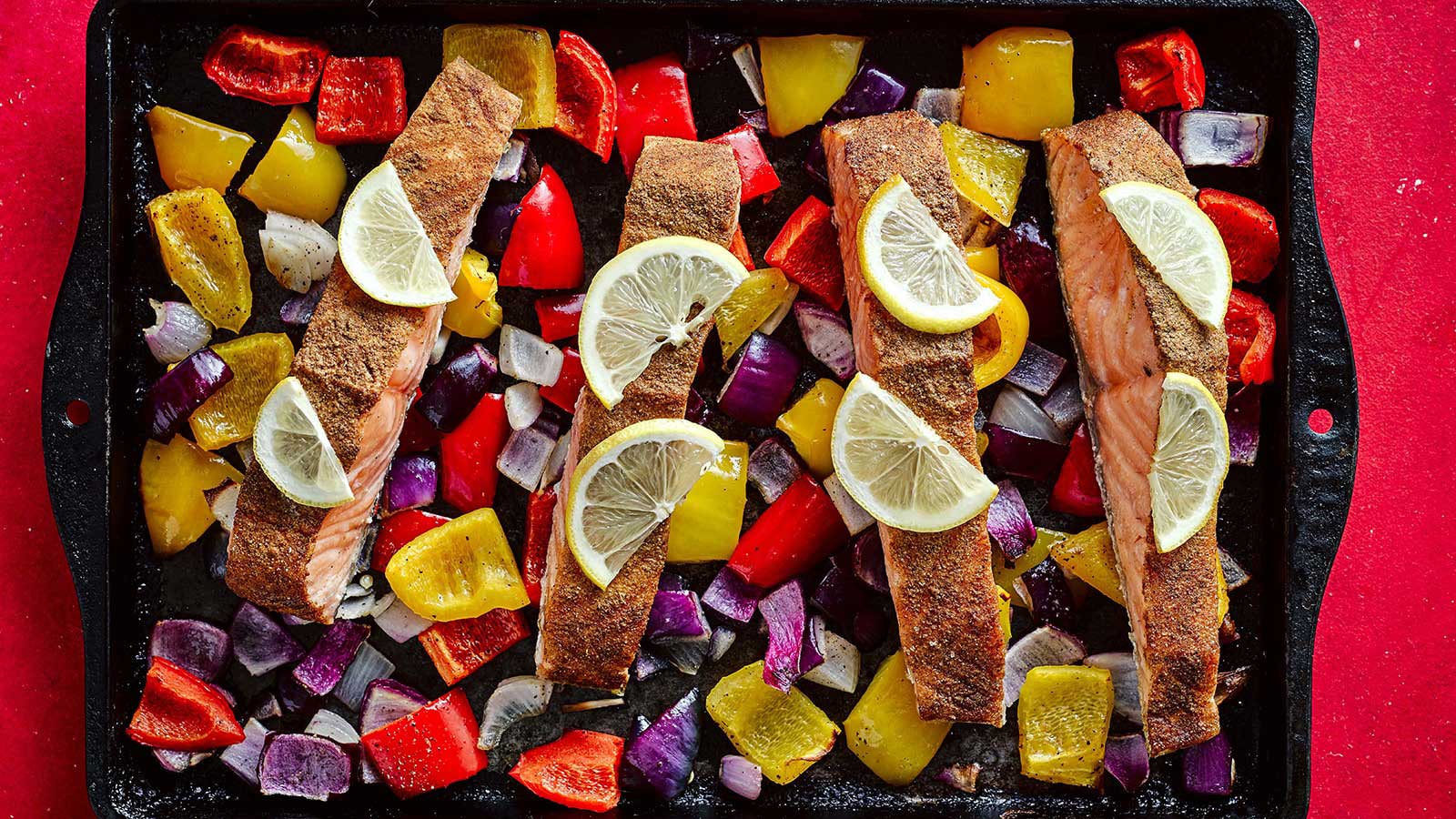 4 fillets of salmon surrounded by peppers, and red onion