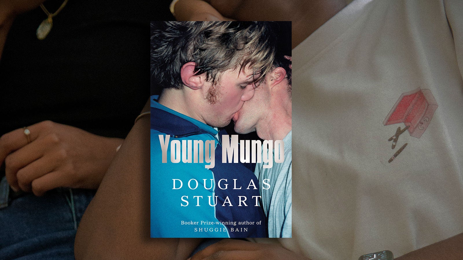 The cover of Young Mungo by Douglas Stuart showing two young men passionately kissing is set against an abstract background showing a young couple cuddling