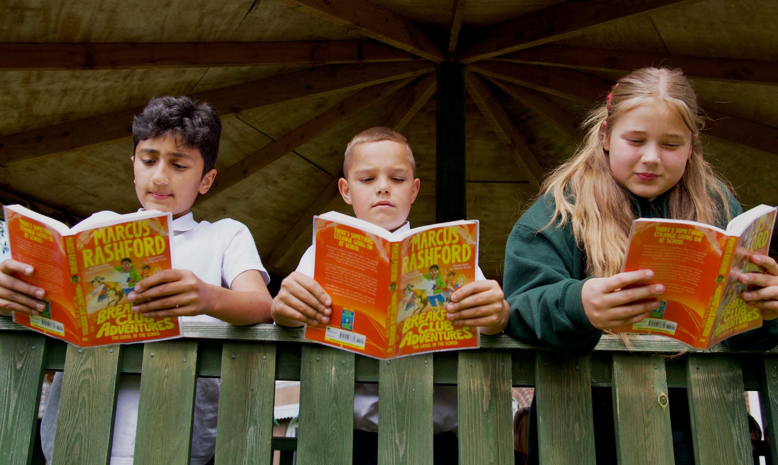 Three children stand in a row reading one of Marcus Rashford's Breakfast Club Adventures