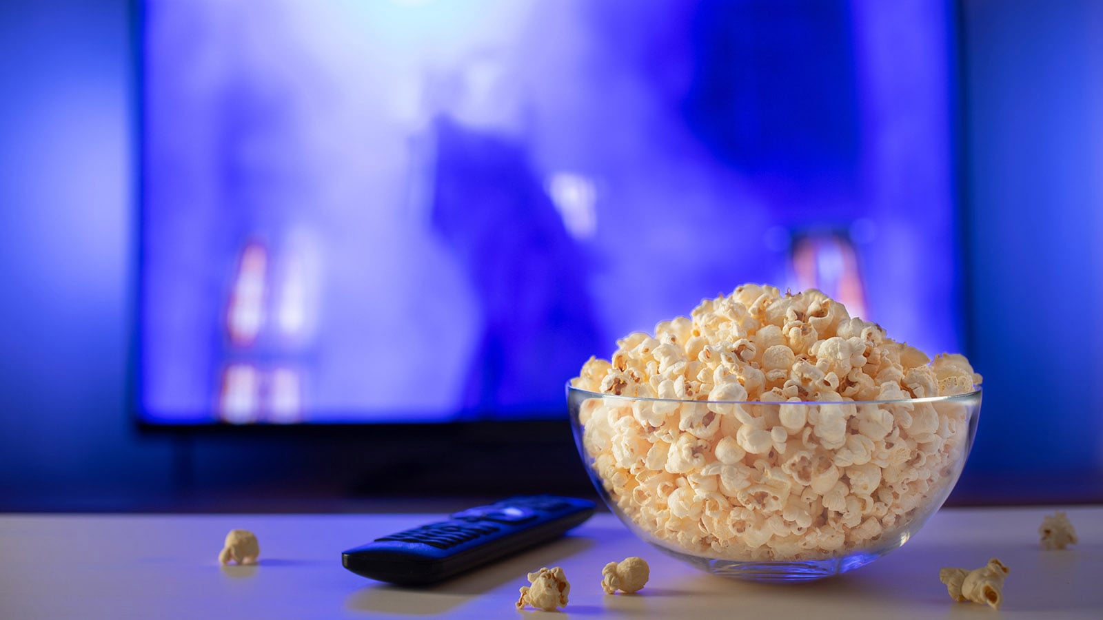Bowl of popcorn and remote on table as film plays in background.