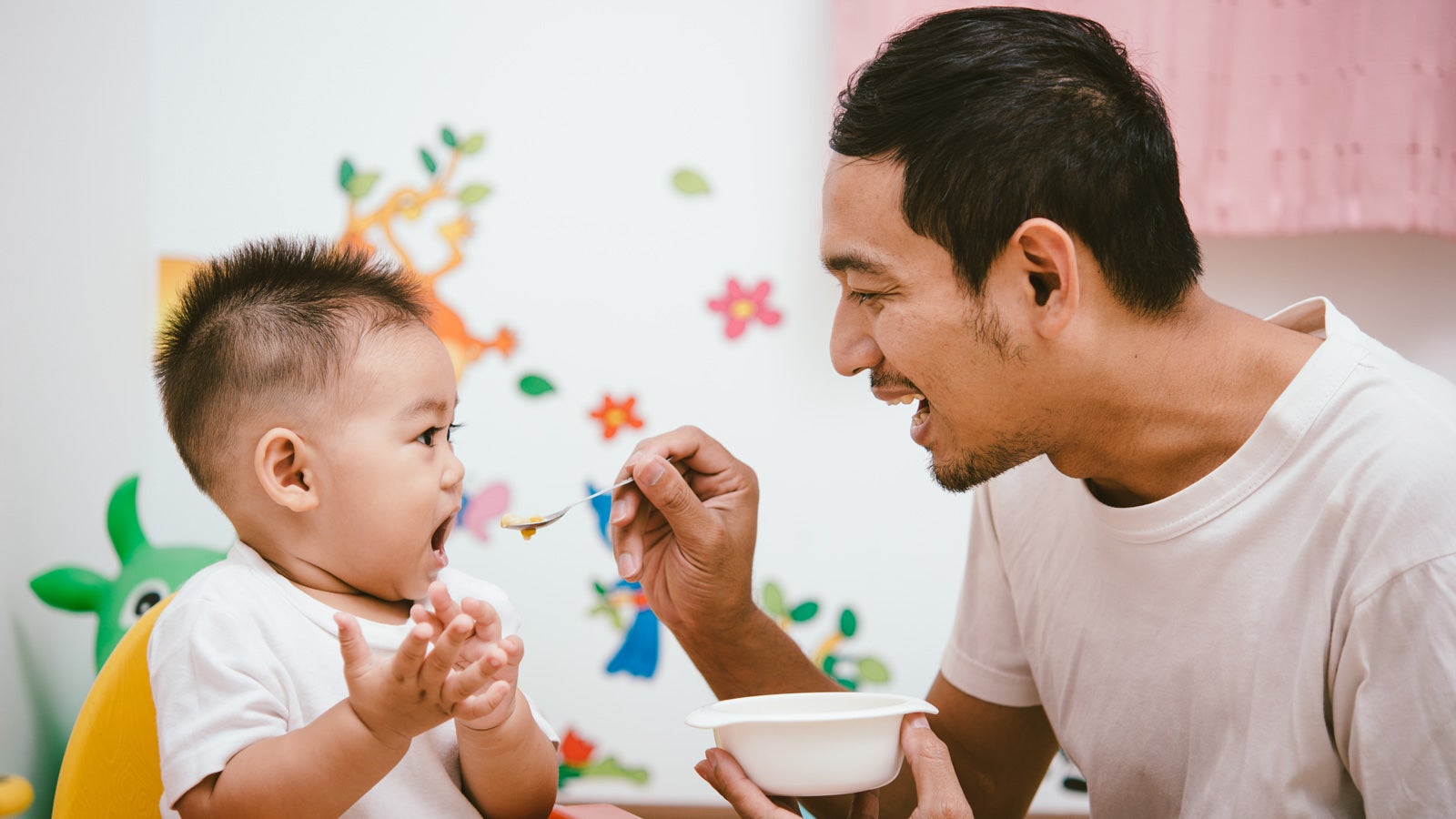 A smiling father feeding his toddler