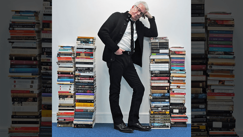 Ken Follett standing with several stacks of books
