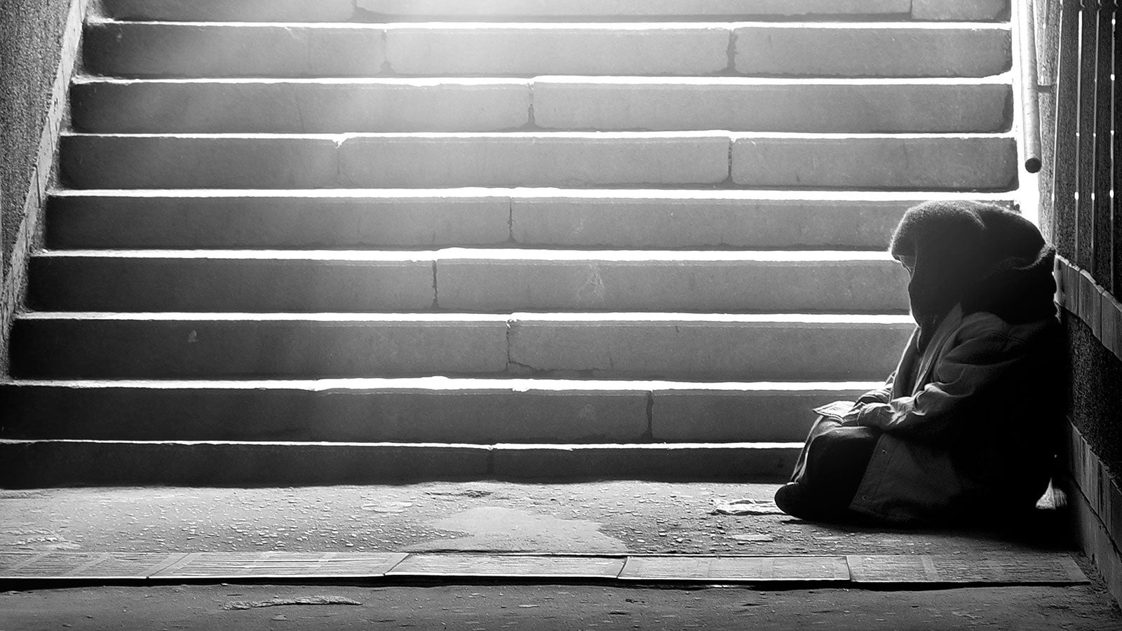 Black and white photo of a homeless woman sat at the bottom of some steps. 