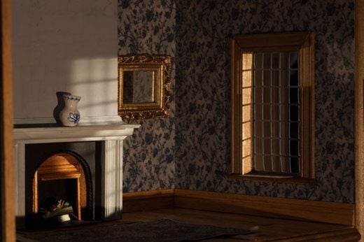 Tiny room including a small fireplace with a blue & white vase on the mantel, a small gold mirror and a window complete with small panes