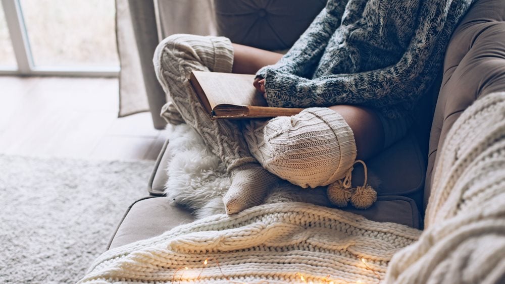 Person sitting on a sofa wearing knitted jumper and socks reading