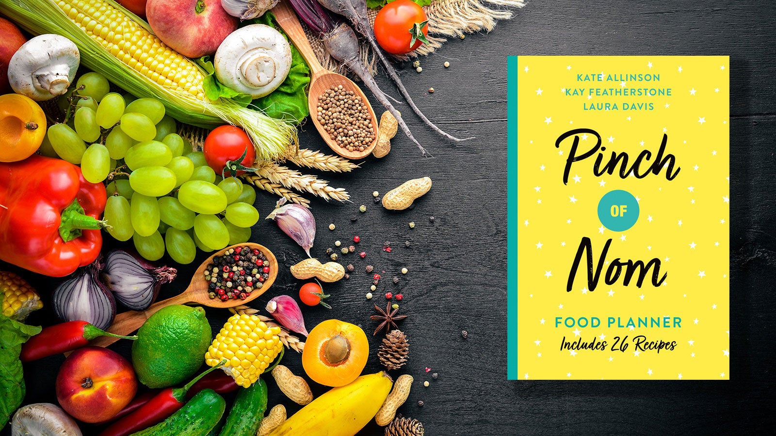 The Pinch of Nom Food Planner set on a black counter next to a pile of fruit and vegetables.