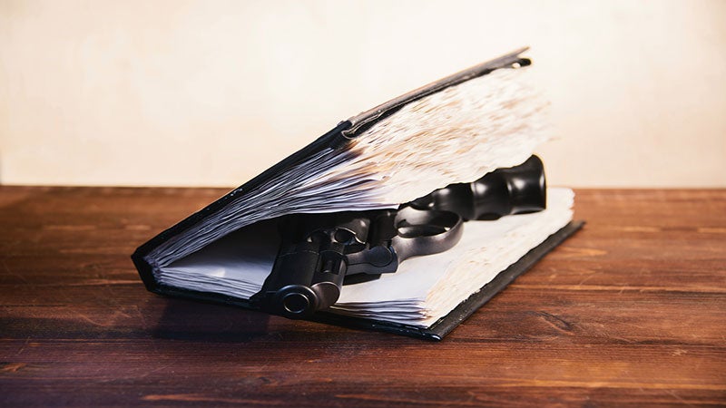 A book lies on a wooden table with a gun between its pages