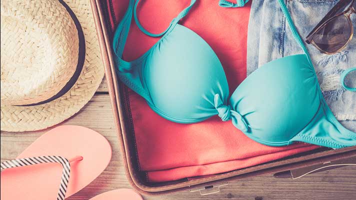 Open suitcase showing summer hat, bikini top, flip-flops and sunglasses