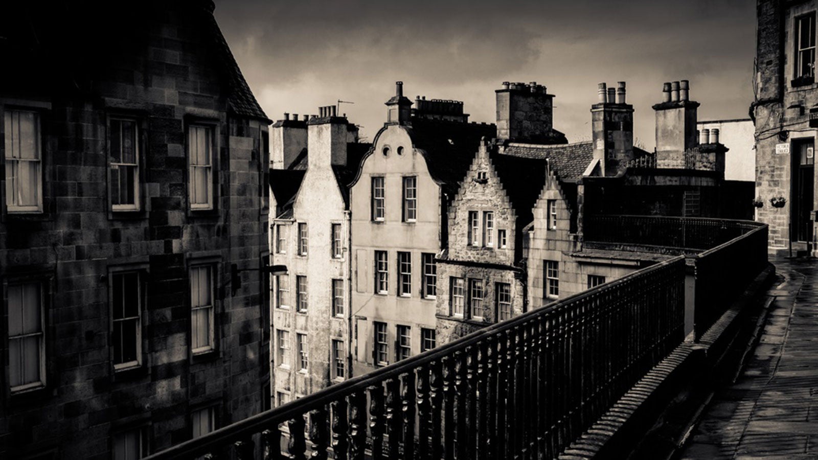 Black and white image of an ancient Edinburgh street under a stormy sky
