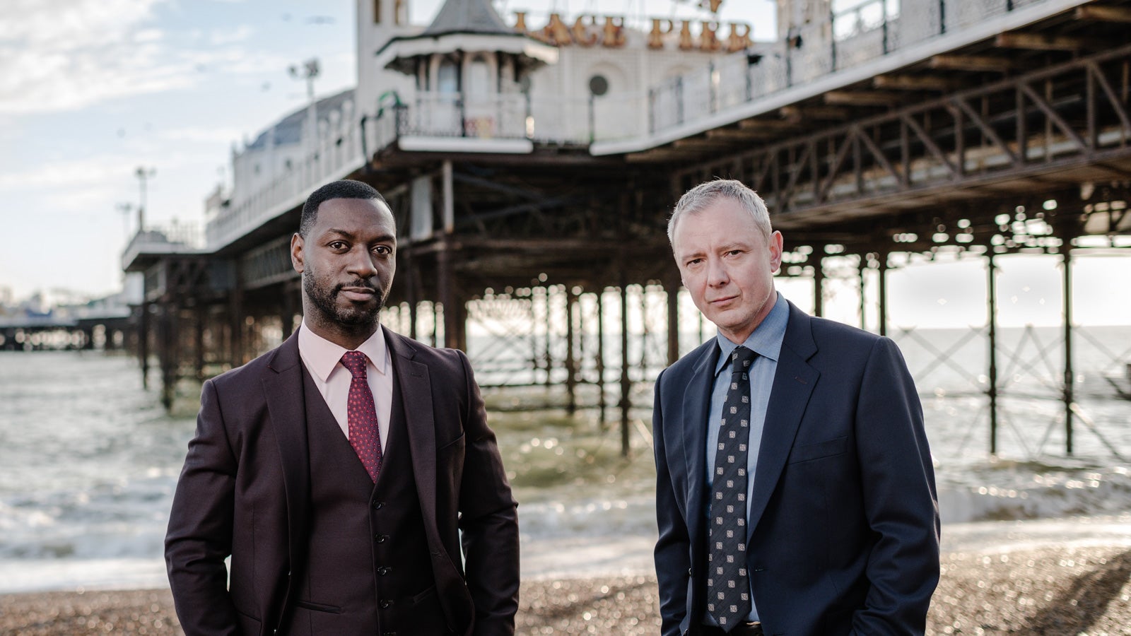 Richie Campbell as Detective Sergeant Glenn Branson and John Simm as detective Superintendent Roy Grace stand in front of Brighton Pier