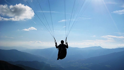 Silhouette of person in parachute against background of mountains and blue sky Silhouette of person in parachute against background of mountains and blue sky