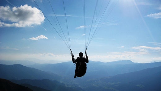 Silhouette of person in parachute against background of mountains and blue sky