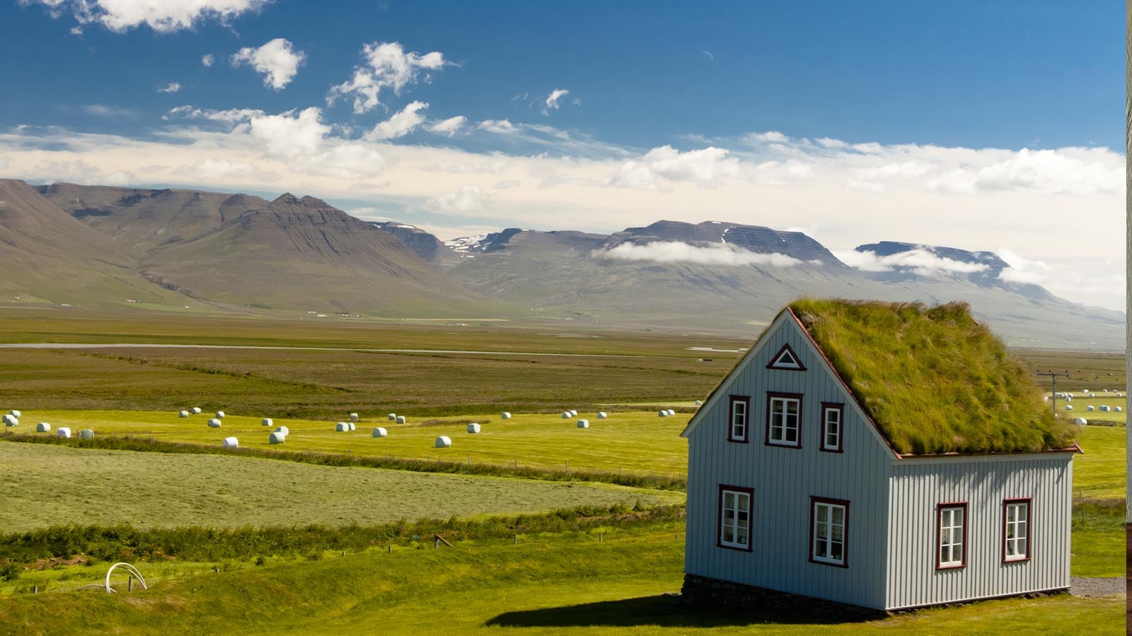 An Icelandic cottage overlooking green fields with mountains in the distance.