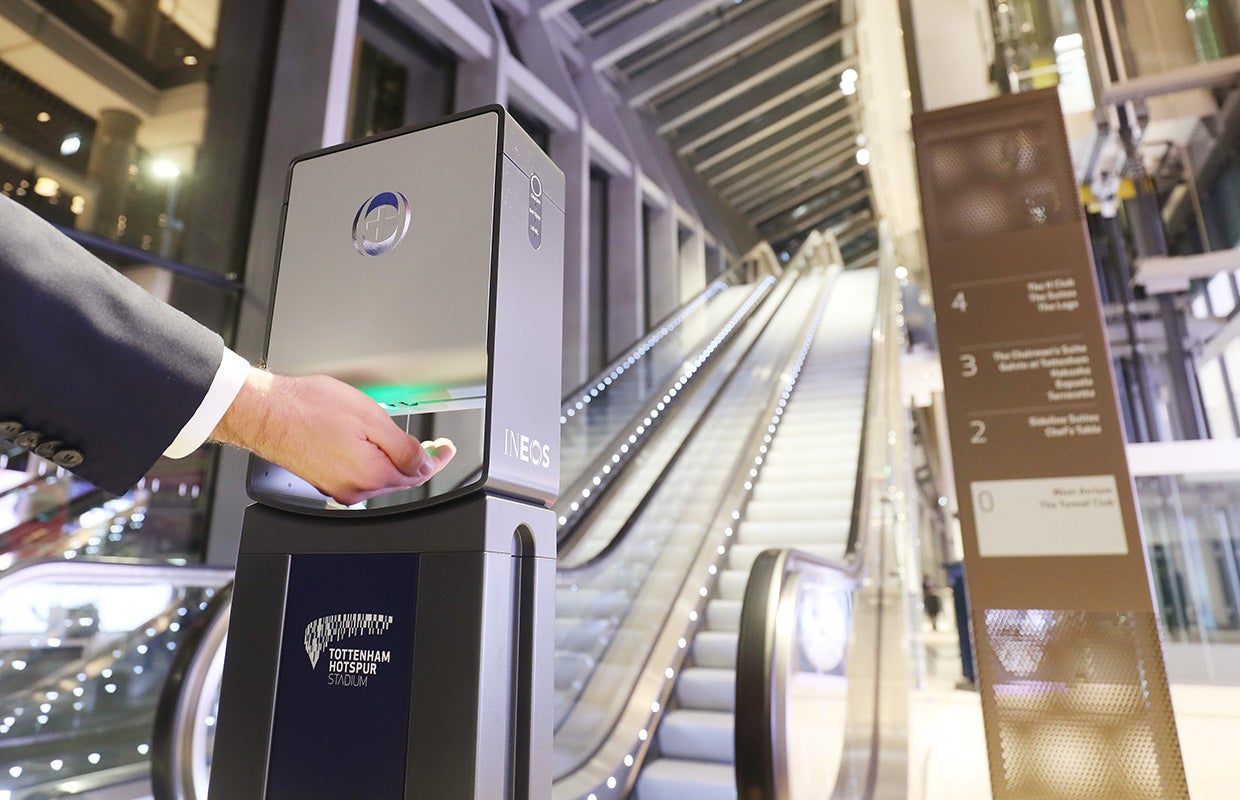 hand triggering sanitiser dispenser next to escalator