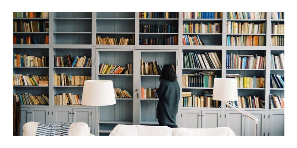 Photo of a lady browsing books on a wall to wall bookshelf