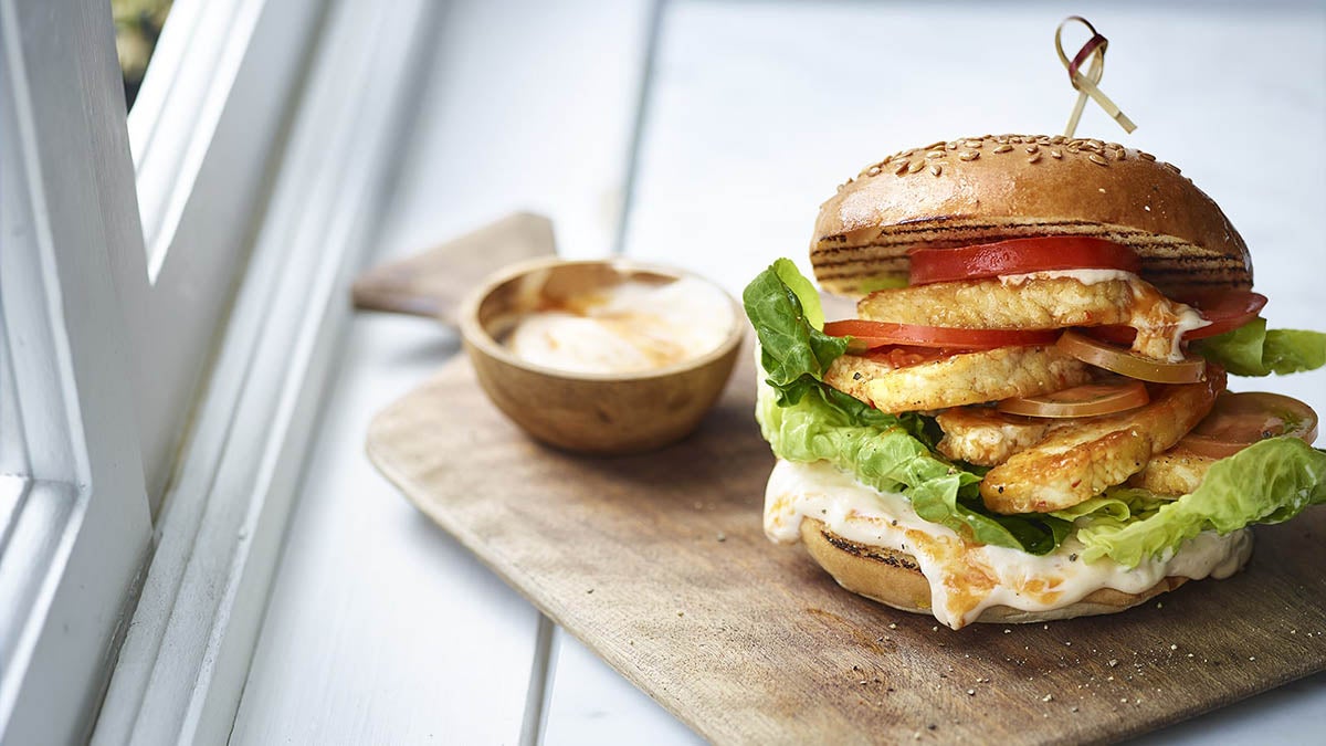 A photo of a Halloumi Burger on a bread board with a side bowl of dip