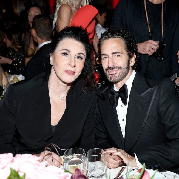 Sue Nabi and Marc Jacobs sit together at a dinner table, smiling at the camera. Sue Nabi wears a black blazer, and Marc Jacobs next to her wears a black tuxedo with a bow tie. Elegant table settings and other guests can be seen in the background. Sue Nabi and Marc Jacobs sit together at a dinner table, smiling at the camera. Sue Nabi wears a black blazer, and Marc Jacobs next to her wears a black tuxedo with a bow tie. Elegant table settings and other guests can be seen in the background.
