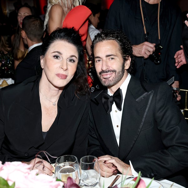Sue Nabi and Marc Jacobs sit together at a dinner table, smiling at the camera. Sue Nabi wears a black blazer, and Marc Jacobs next to her wears a black tuxedo with a bow tie. Elegant table settings and other guests can be seen in the background. Sue Nabi and Marc Jacobs sit together at a dinner table, smiling at the camera. Sue Nabi wears a black blazer, and Marc Jacobs next to her wears a black tuxedo with a bow tie. Elegant table settings and other guests can be seen in the background.
